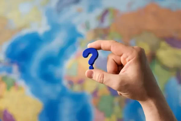 Adult hand holding question mark plastic toy on the world political map background. Travel planning explore destination concept. Quarantine over, borders open